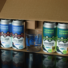Load image into Gallery viewer, A cardboard shipping box containing four Firebrand Brewing cans and a clear glass, photographed from above on a reflective surface.
